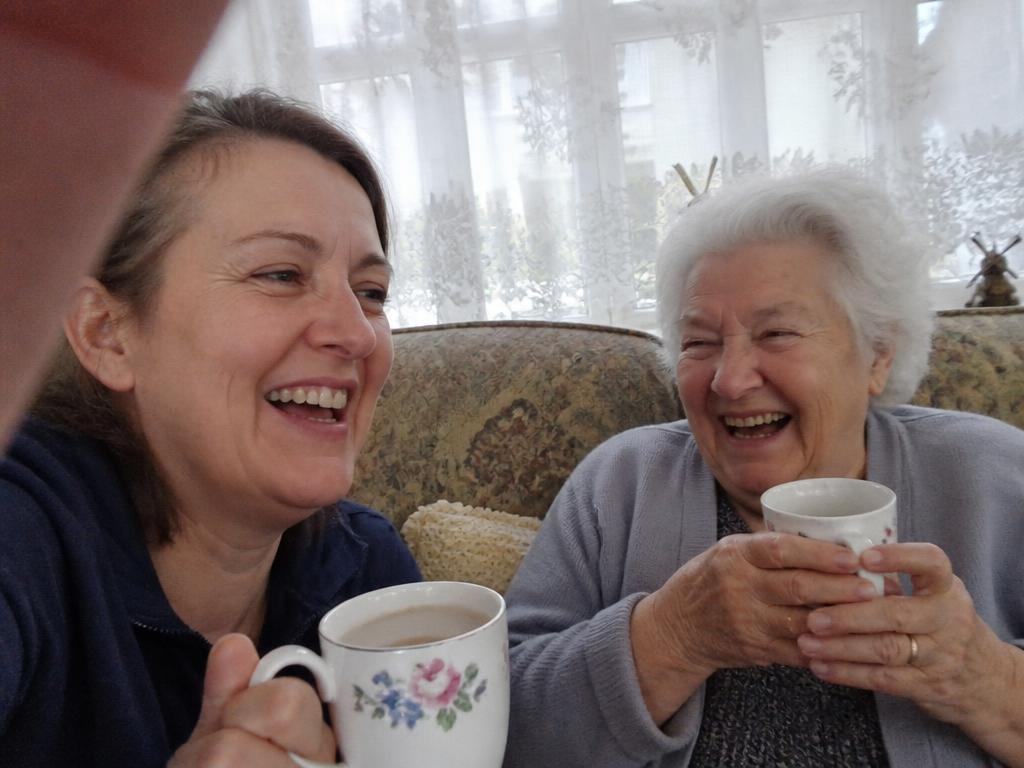 A daughter and her mother laughing together over tea
